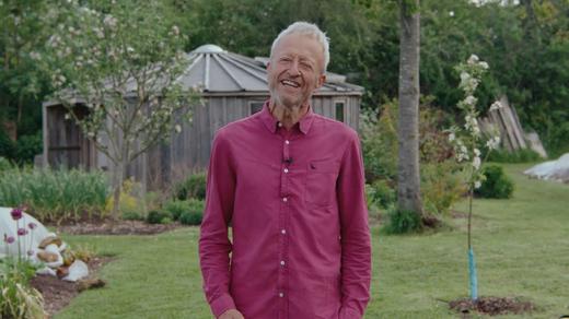 An established Roots site with young trees, planted beds and chickens, and a member standing among them