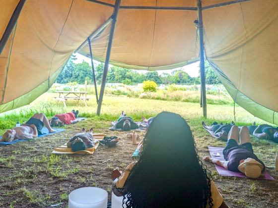 People lying on mats doing yoga inside the tipi, looking out over the site