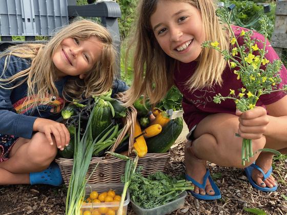 Two girls crouched by a basket of courgettes and tomatoes, one holding cut flowers