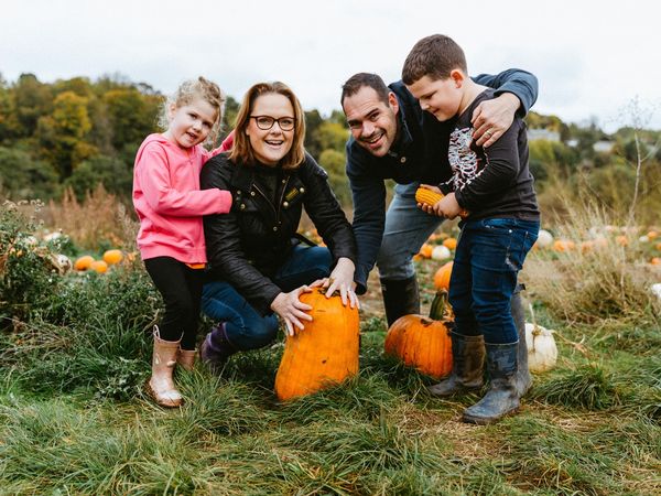 A family of four crouched together in a pumpkin patch